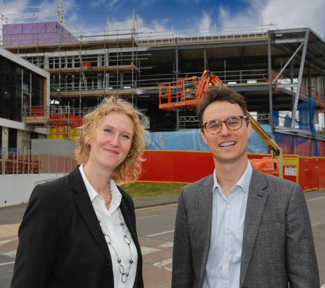 Two individuals stand before a building under construction